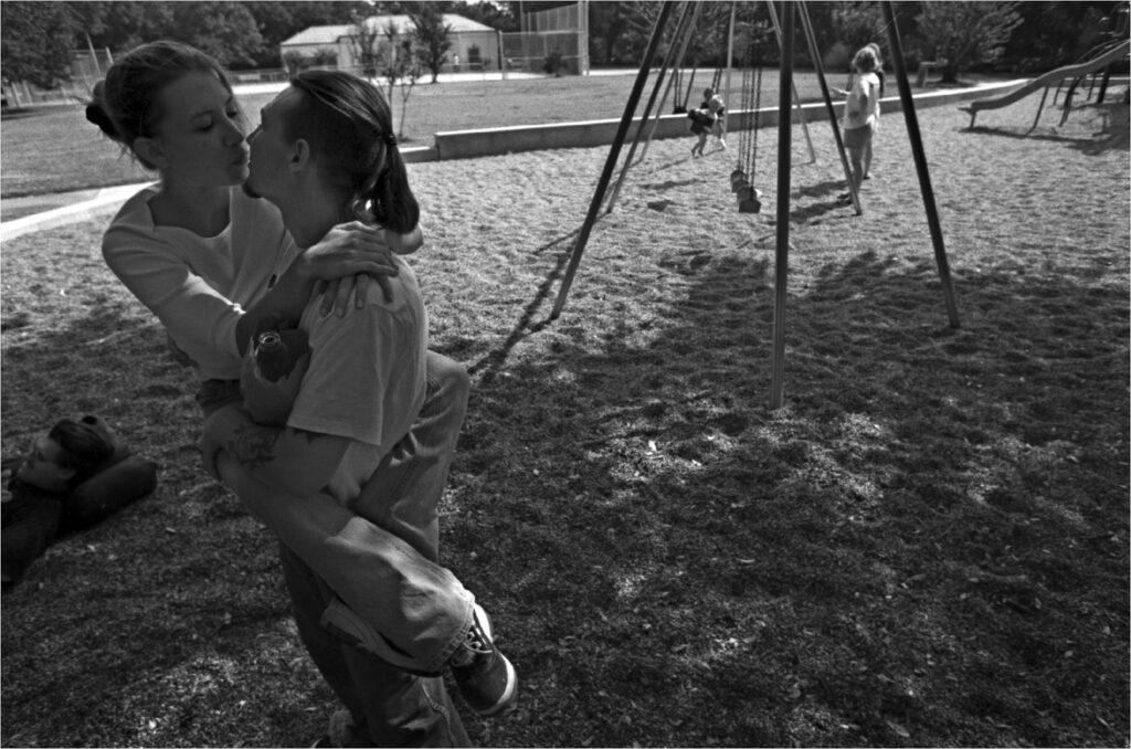 With mothers and their children in the background at this park in Houston Joe Calzada kisses his wife Jennifer near Montrose and West Gray tuesday Sept. 21, 1999. Unusual for street people, Joe and Jennifer got married. They were still practically newlyweds when this photo was taken in a Montrose park.